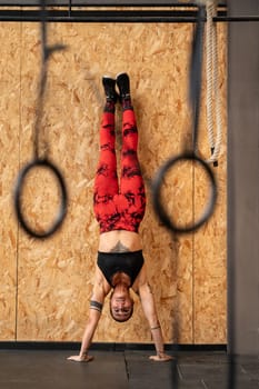 Vertical photo of a sportive mature woman performing handstand exercise in the gym