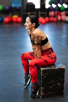 Vertical side view photo of a mature athlete resting sitting on a box in a gym