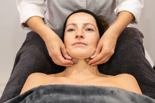 High angle of crop anonymous cosmetician massaging neck of woman with crystals during rejuvenation procedure in beauty clinic