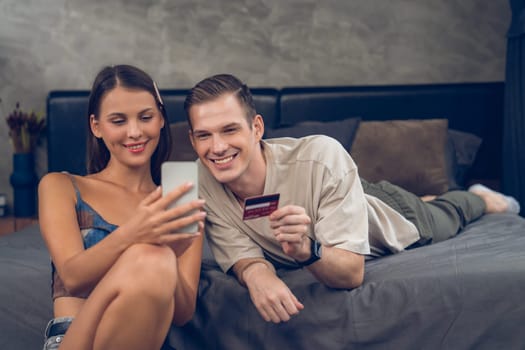 Young couple sit in the home bedroom using online payment app and digital wallet on smartphone to pay with credit card. E commerce shopping and modern purchasing via mobile internet. Unveiling