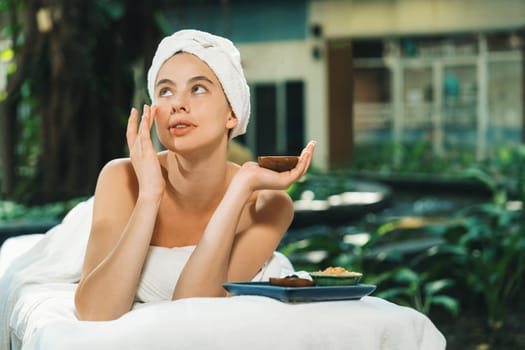 Beautiful caucasian women in white towel smells herbal homemade facial mask while lie on spa bed surrounded by outdoor natural environment. Relaxing and chilling concept. Tranquility.