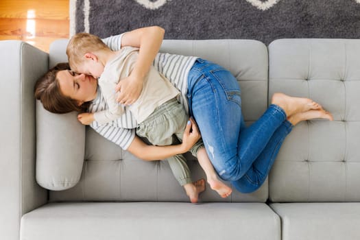 Mother and child cuddling on a grey sofa. Indoor casual lifestyle portrait. Family and love concept. Design for greeting card, poster