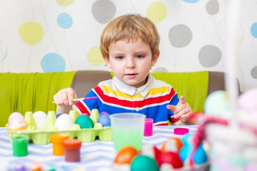 Happy Easter. Kid is dyeing Easter eggs. Boy dyes colorful egg for Easter hunt