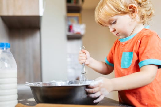 Cute little boy makes baking dough in the kitchen at home.