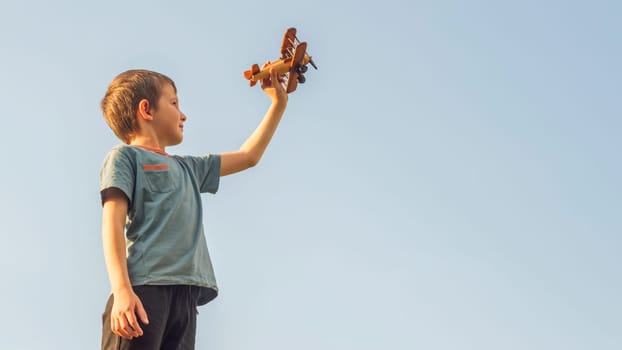 Happy kid playing with toy wooden airplane against sky background. Concept of educations, future, business, international and travel