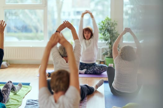 A group of senior women engage in various yoga exercises, including neck, back, and leg stretches, under the guidance of a trainer in a sunlit space, promoting well-being and harmony.