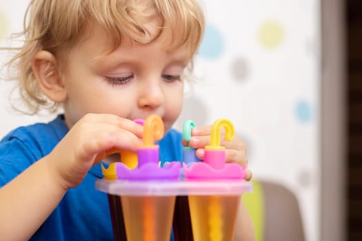 Child making ice cream from fruit juice on table at home.