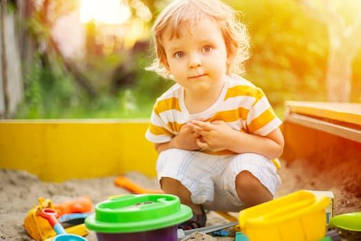 A little boy playing in the sandbox at the playground outdoors. Toddler playing with sand molds and making mudpies. Outdoor creative activities for kids.