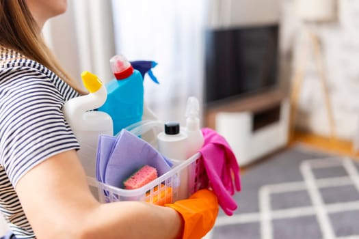 Woman in rubber gloves with basket of cleaning supplies ready to clean up her apartment. Housewife has many household chores, domestic work and professional cleaning service. Low depth of field