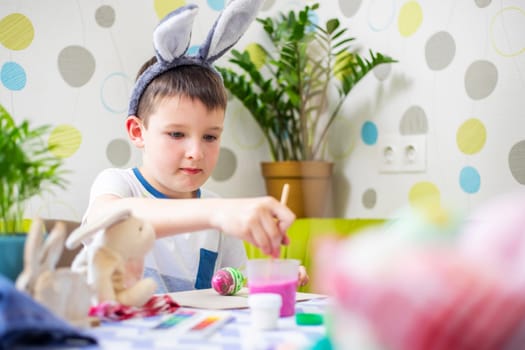 Happy Easter. Kid is dyeing Easter eggs. Boy in bunny ears dyes colorful egg for Easter hunt