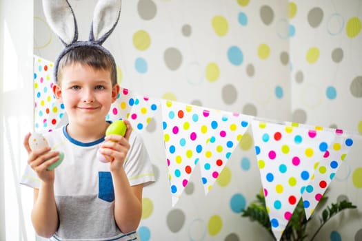 Cute boy with bunny ears holding Easter eggs. Happy child preparing for Easter