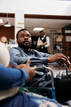 Young African American man on wheelchair arriving at luxury hotel with disabled facilities, handicapped guy traveling with wife. Accessible tourism, travel accommodation and disability