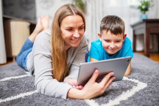 Happy loving family. Young mother and her son using tablet pc lying on carpet. Funny mom and lovely child are having fun at home