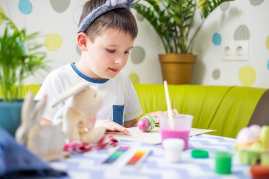 Happy Easter. Kid is dyeing Easter eggs. Boy in bunny ears dyes colorful egg for Easter hunt