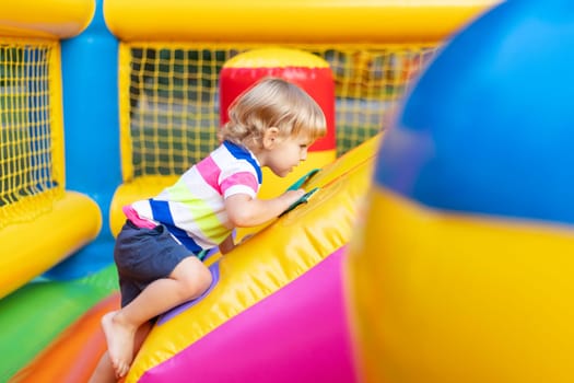 Happy kid having fun on colorful inflatable attraction playground. Child have fun and ride on the outdoor playground.