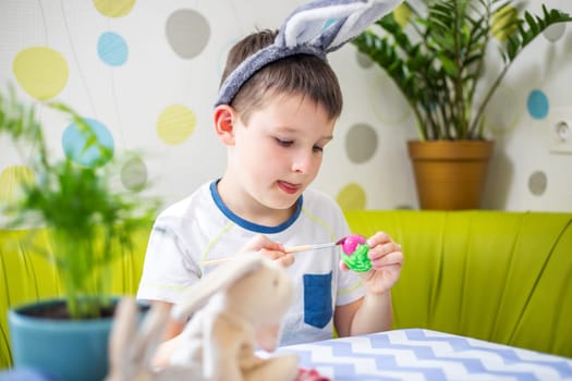 Happy Easter. Kid is dyeing Easter eggs. Boy in bunny ears dyes colorful egg for Easter hunt