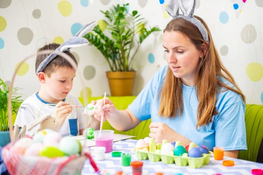 Happy Easter. A mother and her son painting Easter eggs. Happy family getting ready for Easter. Mom and child boy wearing bunny ears on Easter day