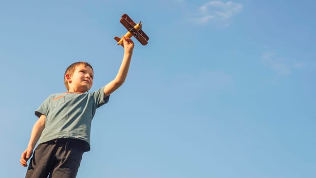 Happy kid playing with toy wooden airplane against sky background. Concept of educations, future, business, international and travel