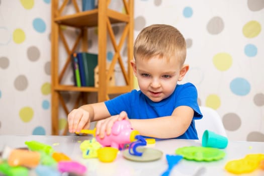 Kid playing with play dough. Cute child sitting at the table and plays with playdough. Creative leisure activity concept.