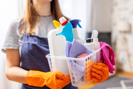 Woman in rubber gloves with basket of cleaning supplies ready to clean up her apartment. Housewife has many household chores, domestic work and professional cleaning service. Low depth of field