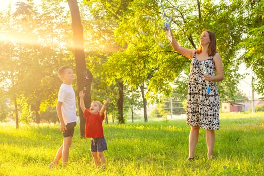 Happy mother and her children are playing with soap bubbles in the park.