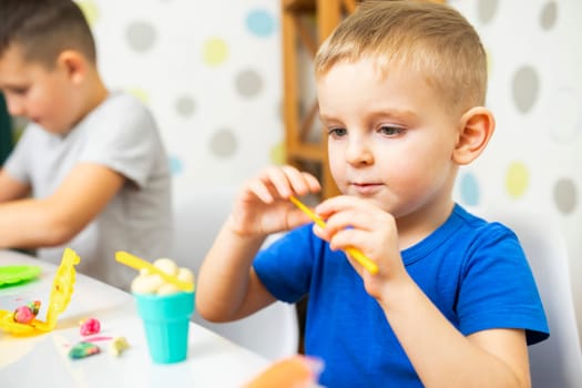 Kids playing with play dough. Cute children sitting at the table and plays with playdough. Creative leisure activity concept