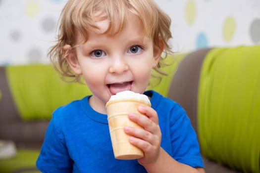 Happy little child in blue t-shirt eating ice cream at home.