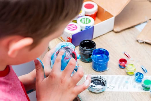 Kid is dyeing Easter eggs. The boy is sitting at the table and enthusiastically engaged in creativity, preparing for Easter.