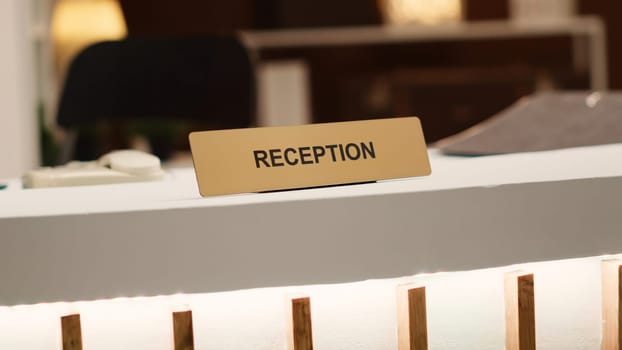 Blurry revealing extreme close up shot of reception sign on empty clean desk in stylish hotel lounge interior. Warm cozy rustic hospitality industry resort check in counter