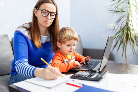 Young woman working at home with a laptop with a child on her lap. Home office with kids. Mother is working from home
