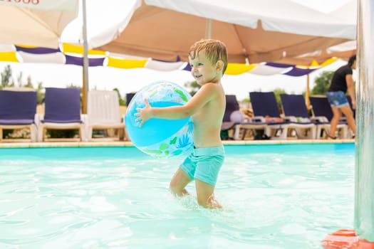 Child resting in swimming pool. Kid swim, dive, leisure and playing with inflatable ball in pool at summer vacation