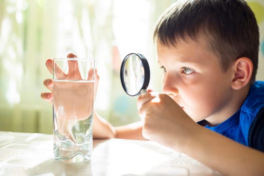 The child boy looking at water in a glass through magnifying glass. Water quality check concept.