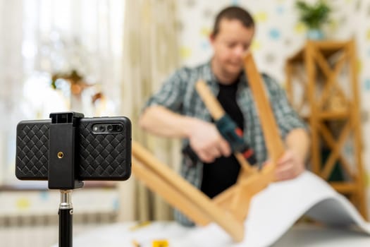 Handyman blogger shows assembling chair, shooting video instructions on smartphone . Man assembling furniture by yourself. Blog about carpentry