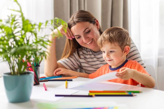 Mother and child drawing with pencils sitting at the desk at home. Happy family