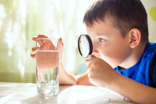 The child boy looking at water in a glass through magnifying glass. Water quality check concept.