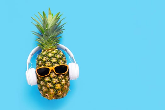 Ripe pineapple with sunglasses and headphones on blue background. Copy space