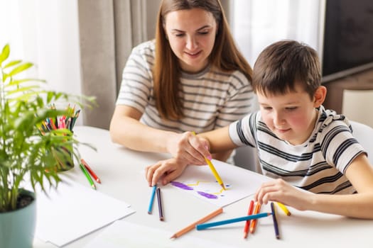 Mother and child drawing with pencils sitting at the desk at home. Happy family