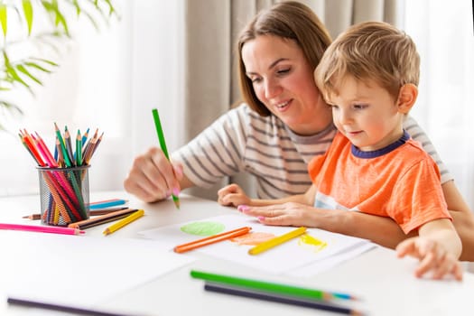 Mother and child drawing with pencils sitting at the desk at home. Happy family