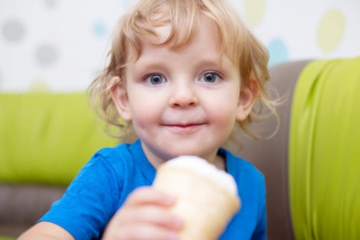 Happy little child in blue t-shirt eating ice cream at home.