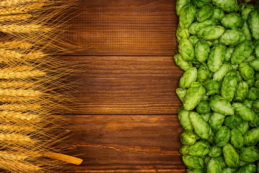 Beer brewing ingredients, green hop cones, and golden wheat ears on a wooden table with space for your object or text