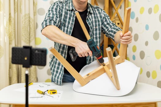 Handyman blogger shows assembling chair, shooting video instructions on smartphone . Man assembling furniture by yourself. Blog about carpentry