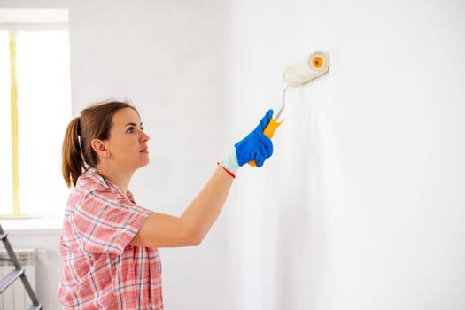Happy woman with roller painting wall in her new apartment. Renovation, redecoration and repair concept