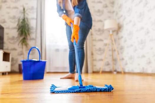 Cropped image of young woman in casual clothes washing a wooden floor with a damp microfiber mop, doing homework, routine cleaning, cleaning job concept