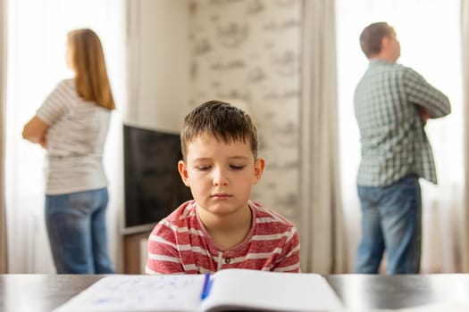 A son feels frustrated while his parents fight in the background. Family conflicts or divorce impact on on child development