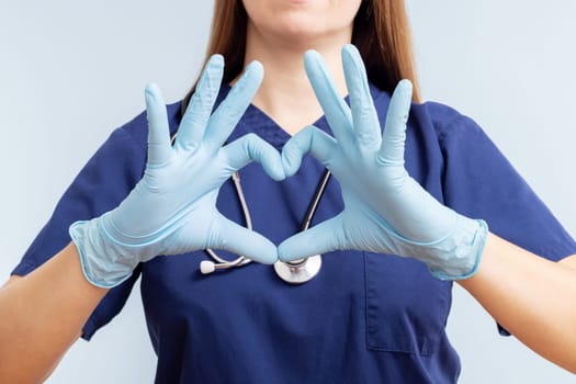 Doctor woman in gloves with a stethoscope doing heart symbol shape with her hands on blue background