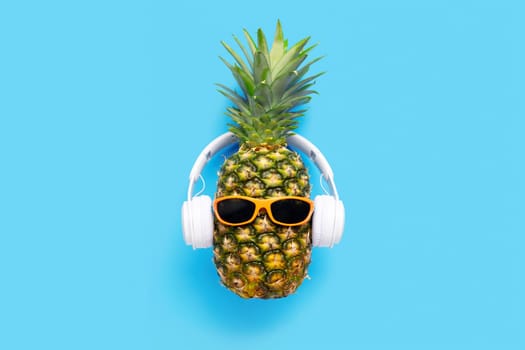 Ripe pineapple with sunglasses and headphones on blue background. Copy space