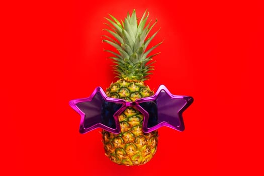 Pineapple with sunglasses on red background. Pineapple in star glasses