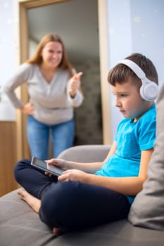 Mother scolds her son. Boy uses tablet computer with headphones and ignores his mom. Family relationships concept