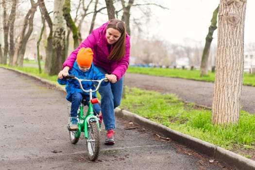 Mother teaching son to ride bicycle. Young mom teaching son to ride bike first time in park. Happy kids on bikes. The best moments together. Childhood bike concept