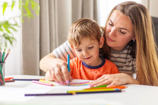 Mother and child drawing with pencils sitting at the desk at home. Happy family